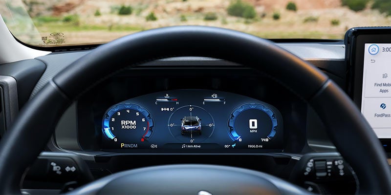 Digital dashboard with RPM and speed at zero, showing a car icon in the center, behind a steering wheel.