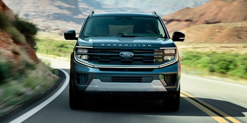 Front view of a blue Ford Expedition SUV driving on a winding road through a desert canyon landscape