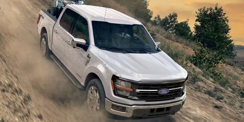 White Ford F-150 pickup truck driving along a dusty off-road trail on a rugged hillside