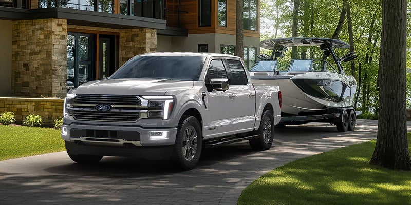 White pickup truck towing a sleek black and white boat on a trailer, parked on a driveway in front of a modern house