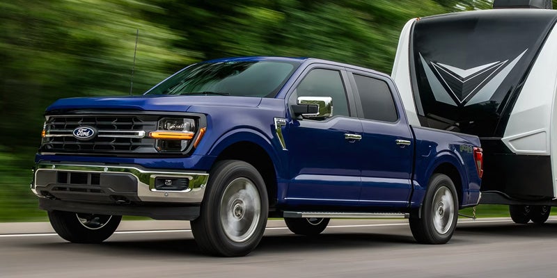 Dark blue Ford F-150 truck pulling a white and black camper trailer on a blurred road